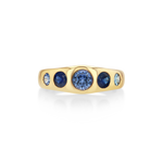 A yellow gold ring featuring a row of round blue gemstones, with a large central deep blue stone and two smaller light blue stones on each side.