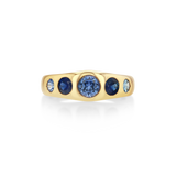 A yellow gold ring featuring a row of round blue gemstones, with a large central deep blue stone and two smaller light blue stones on each side.