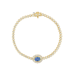 A yellow gold tennis bracelet featuring round-cut clear stones and a central oval blue sapphire surrounded by a halo of small clear stones, displayed on a clean white background.