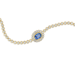 A gold chain bracelet featuring a central oval blue sapphire stone surrounded by a halo of small clear stones, with the rest of the chain lined with round clear stones, shown on a plain white background.