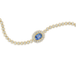 A gold chain bracelet featuring a central oval blue sapphire stone surrounded by a halo of small clear stones, with the rest of the chain lined with round clear stones, shown on a plain white background.