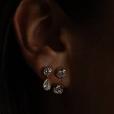 Close-up of an ear wearing two silver earrings against a dark background