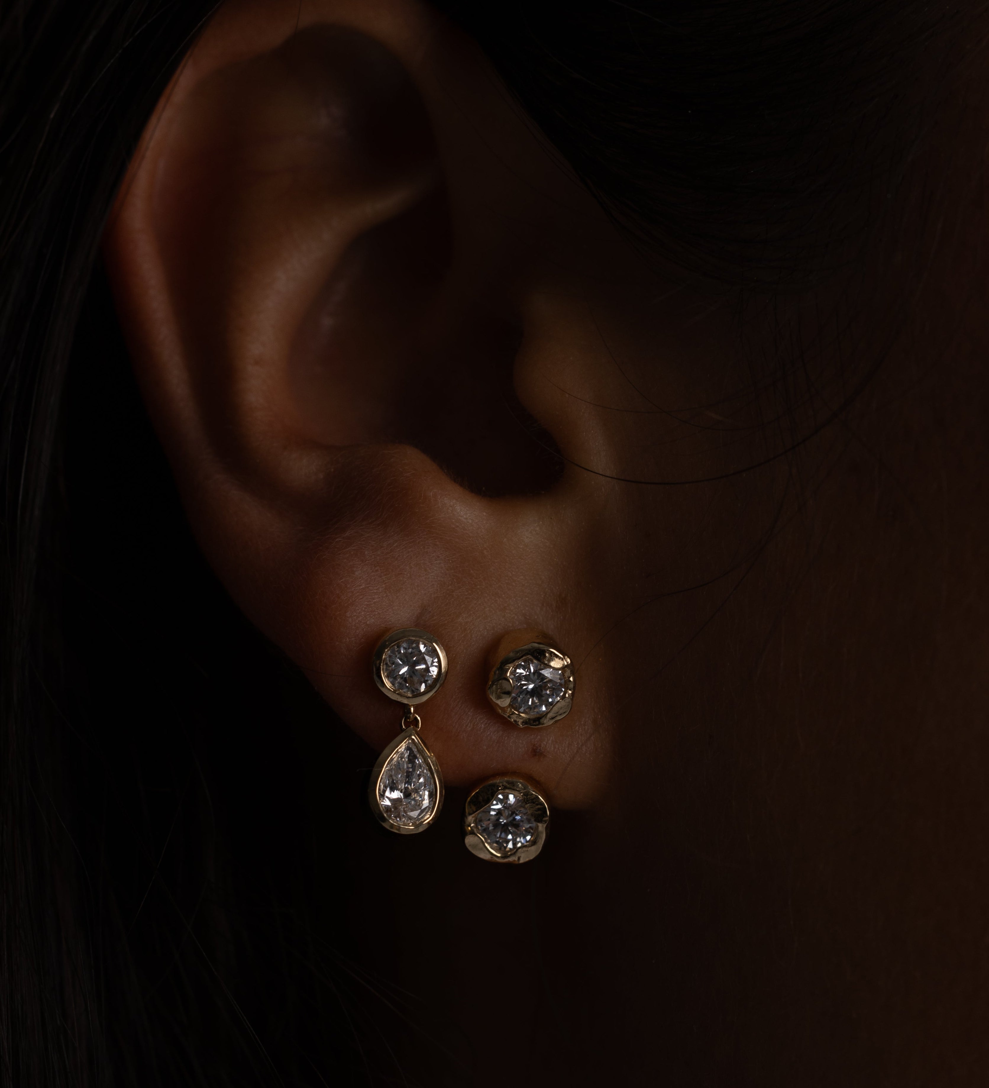 Close-up of an ear wearing two silver earrings against a dark background