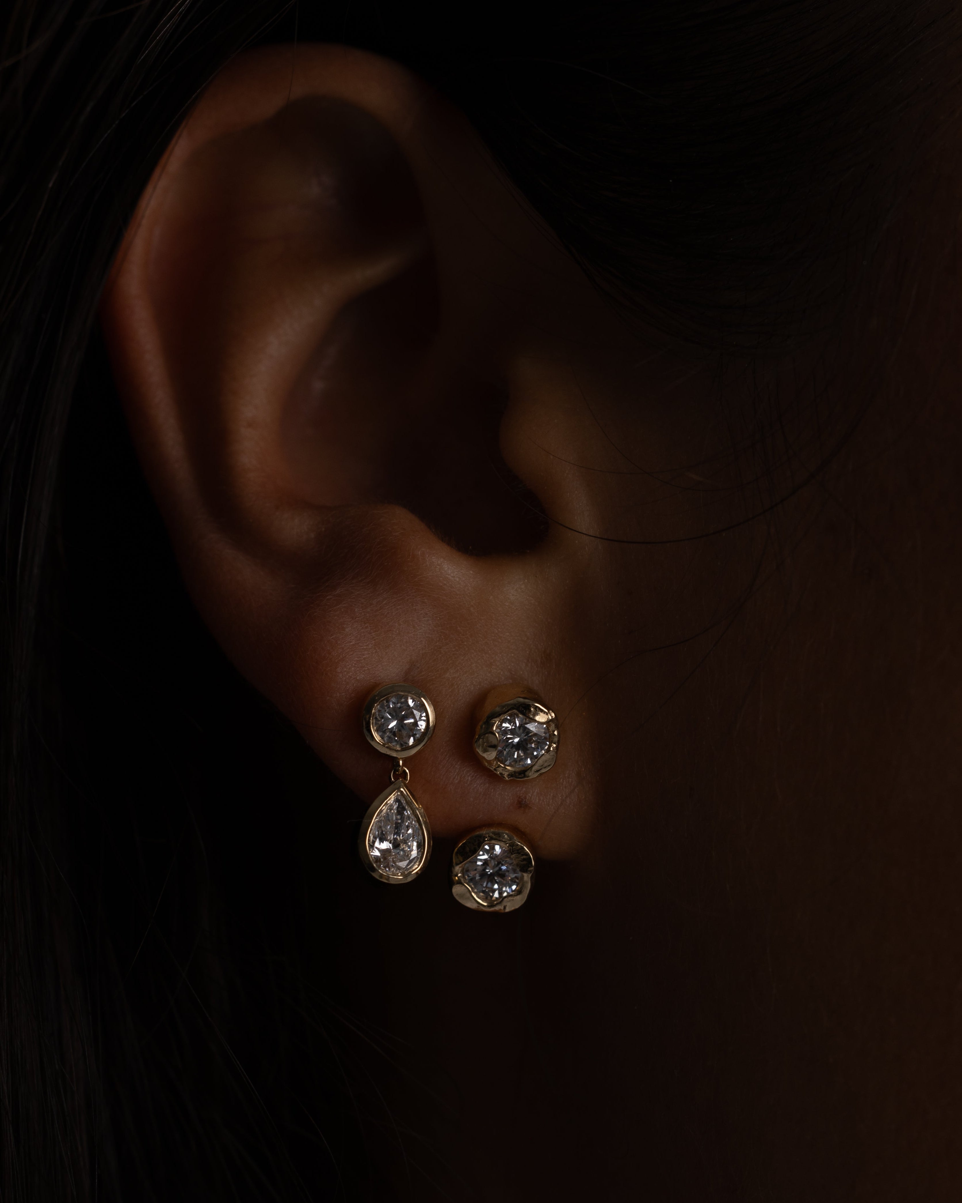 Close-up of an ear wearing two silver earrings against a dark background