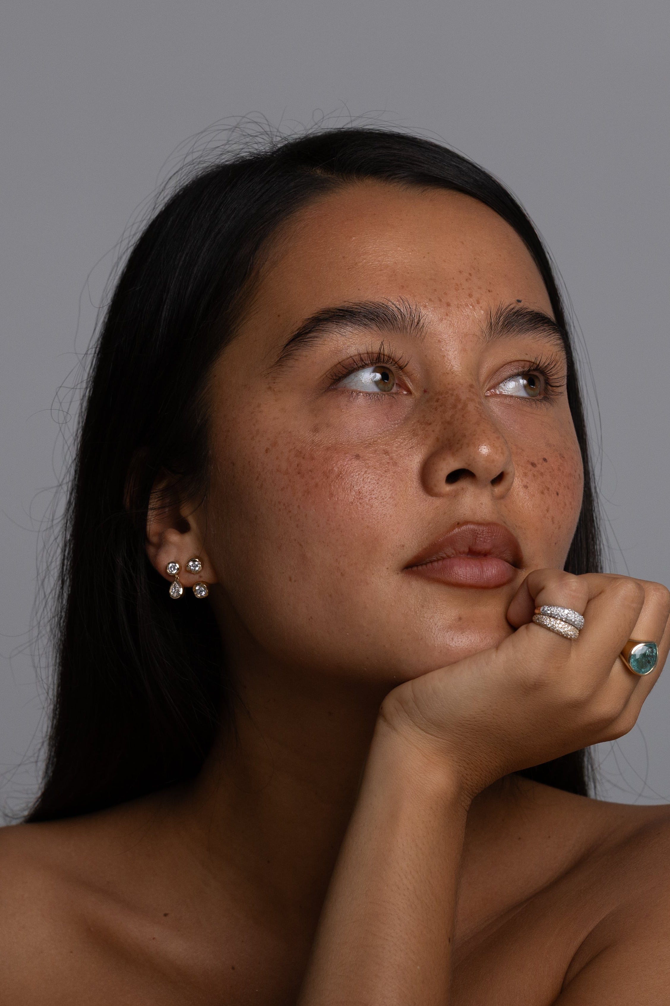Woman with long dark hair and minimal makeup against a gray background