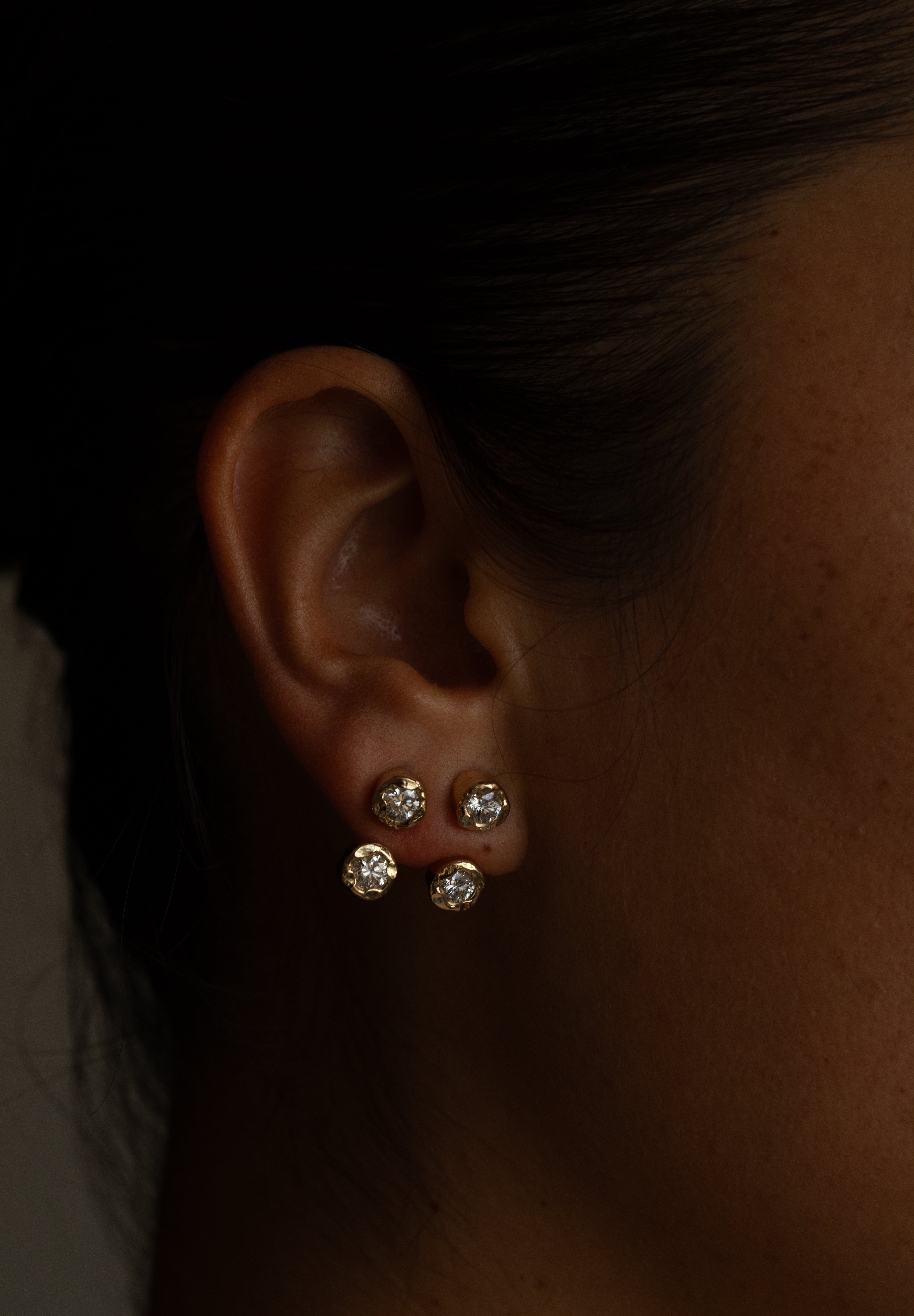 Close-up of an ear wearing three diamond stud earrings.