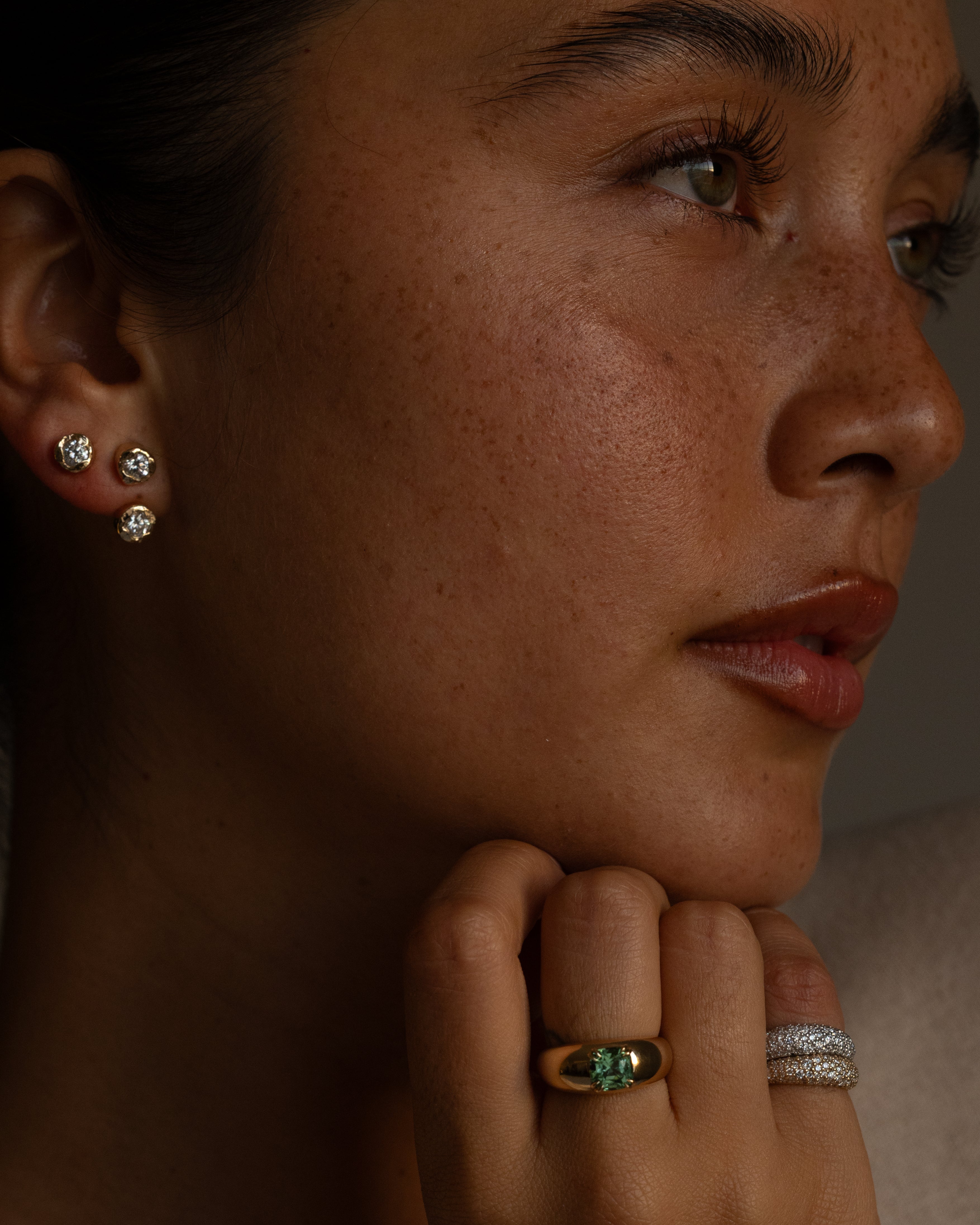 Close-up of a person wearing earrings and rings with a neutral background