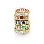 A stack of five gold rings set with multiple colored gemstones, including pink, clear, red, blue, green, and white stones, displayed on a clean white background.