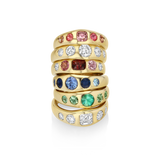 A stack of five gold rings set with multiple colored gemstones, including pink, clear, red, blue, green, and white stones, displayed on a clean white background.