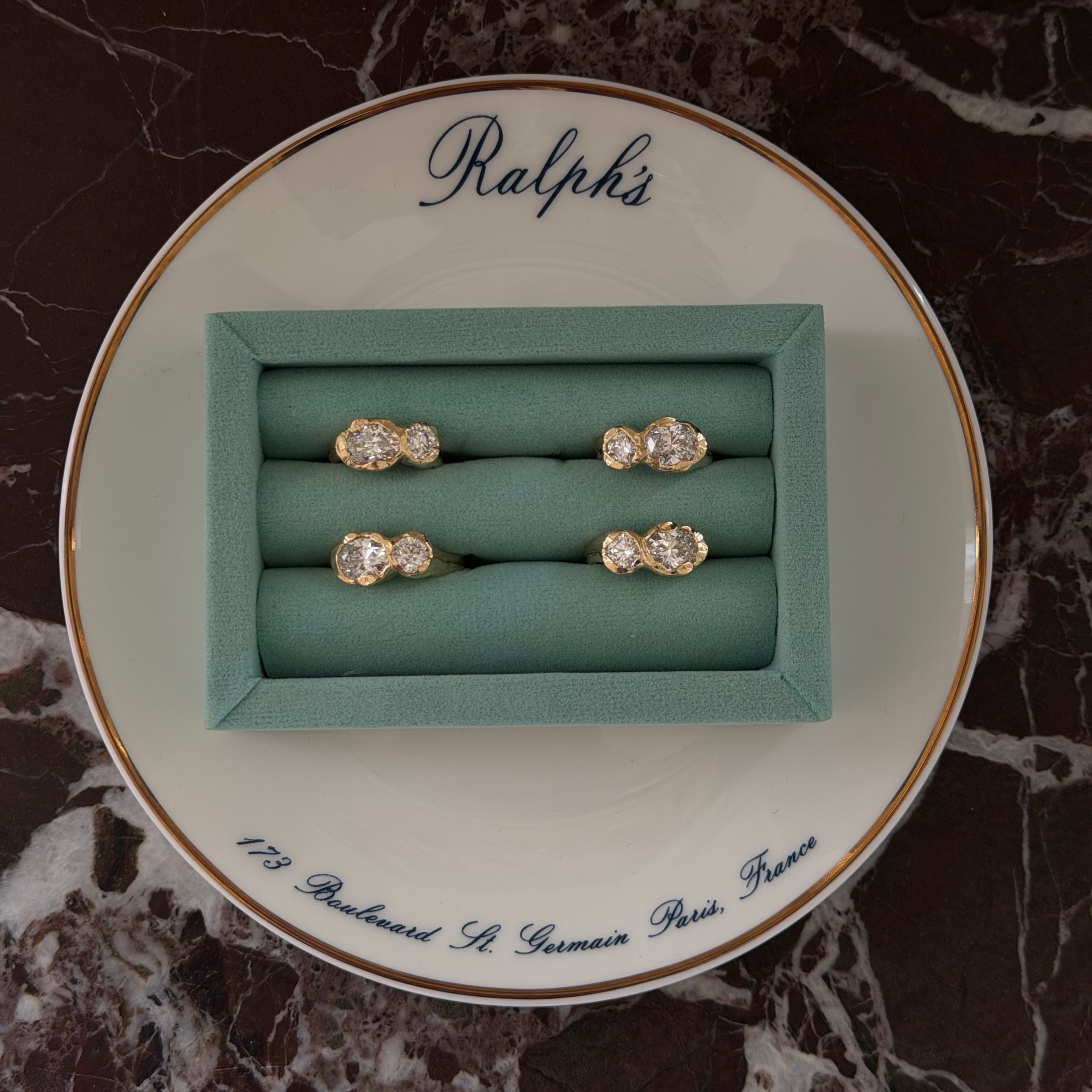 Two diamond rings in a green box on a decorative plate with 'Ralph's' branding.