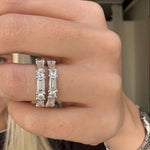 Close-up of a hand wearing two diamond eternity bands with a blurred background.