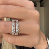 Close-up of a hand wearing two diamond eternity bands with a blurred background.