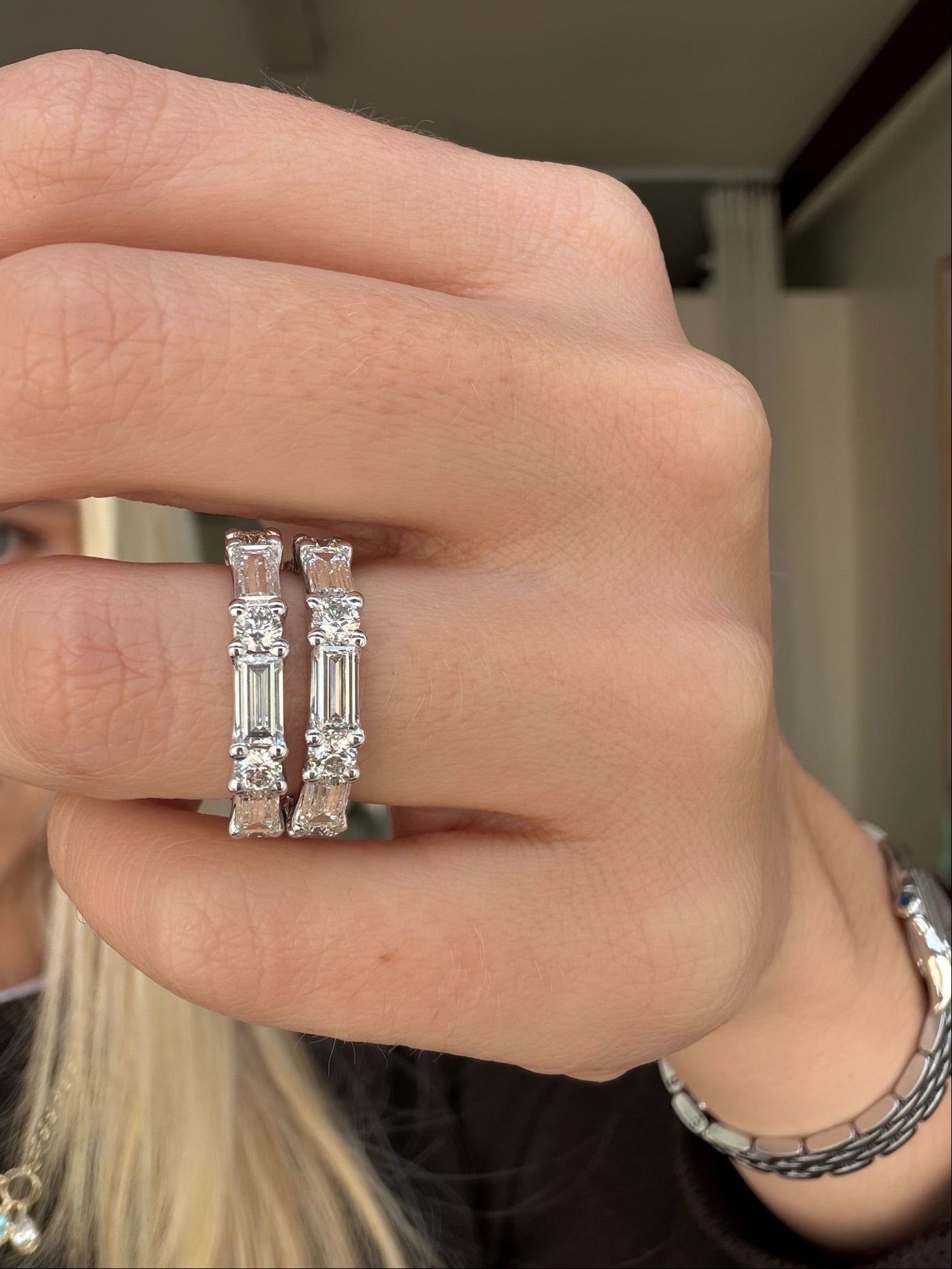 Close-up of a hand wearing two diamond eternity bands with a blurred background.
