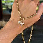 A gold chain hand bracelet with a small pendant featuring a clear faceted gemstone, shown worn on a person's hand with gold rings on the fingers.