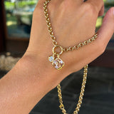 A gold chain hand bracelet with a small pendant featuring a clear faceted gemstone, shown worn on a person's hand with gold rings on the fingers.