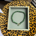 A green beaded necklace with a paraiba green charm hand bezelled in gold inside a velvet box