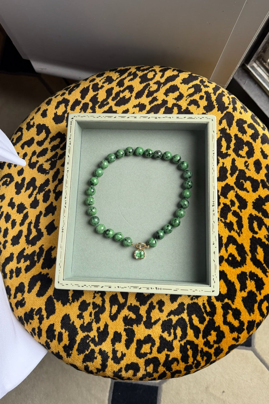 A green beaded necklace with a paraiba green charm hand bezelled in gold inside a velvet box