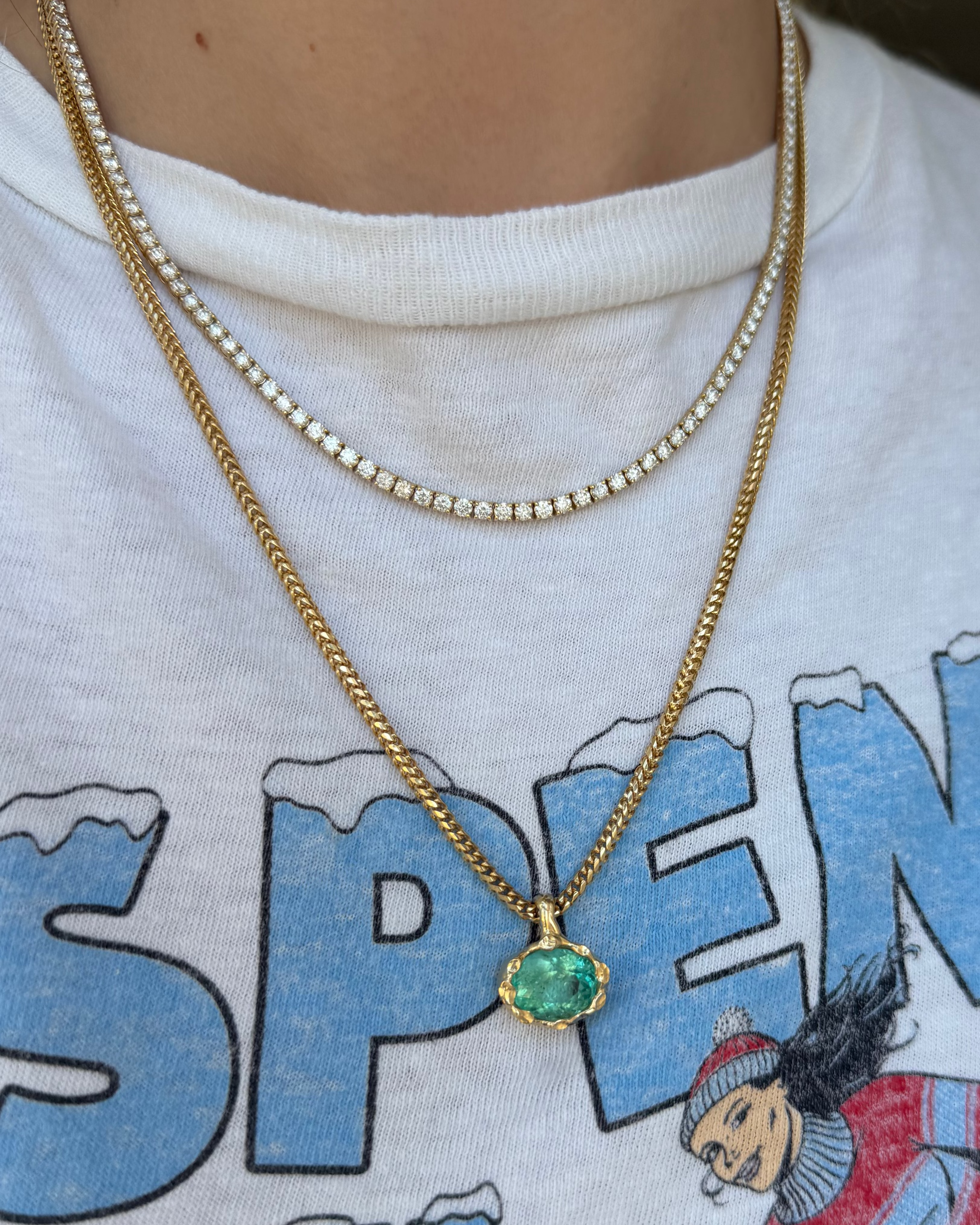 Gold necklace with a green pendant on a white shirt with blue text